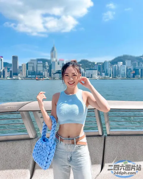 一个女人站在码头上，手里拿着一个蓝色的包，背景是一座城市
