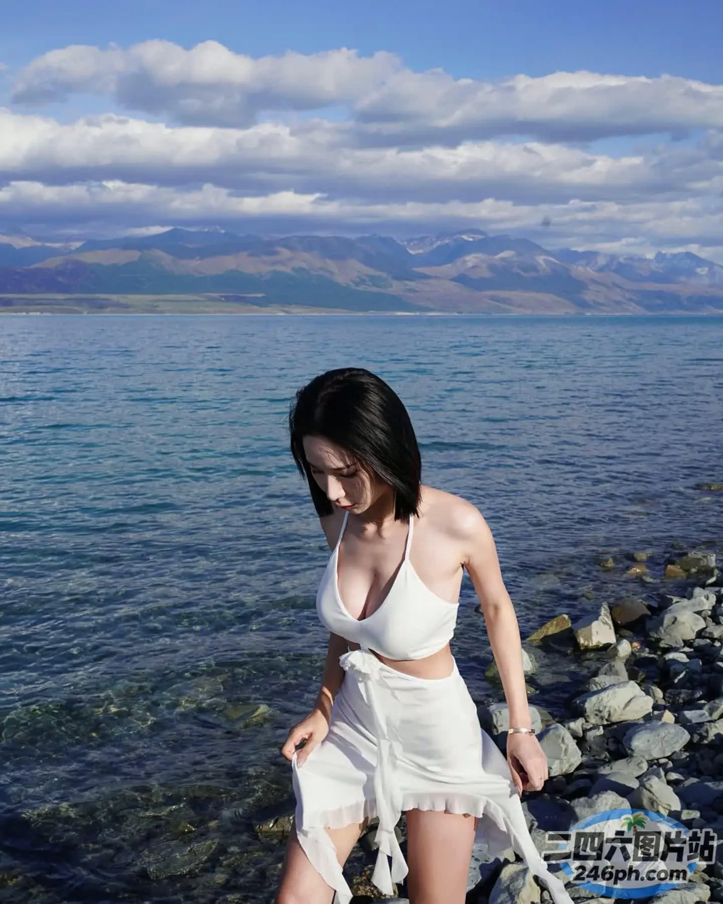 穿着白色连衣裙的 Arafed 女子在水边的岩石海滩上行走