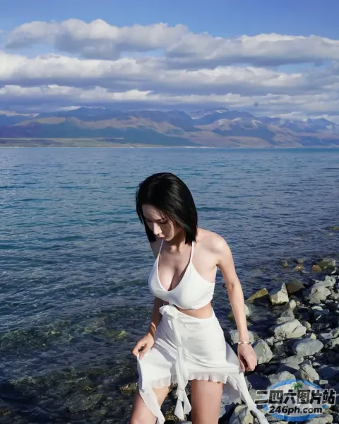 穿着白色连衣裙的 Arafed 女子在水边的岩石海滩上行走
