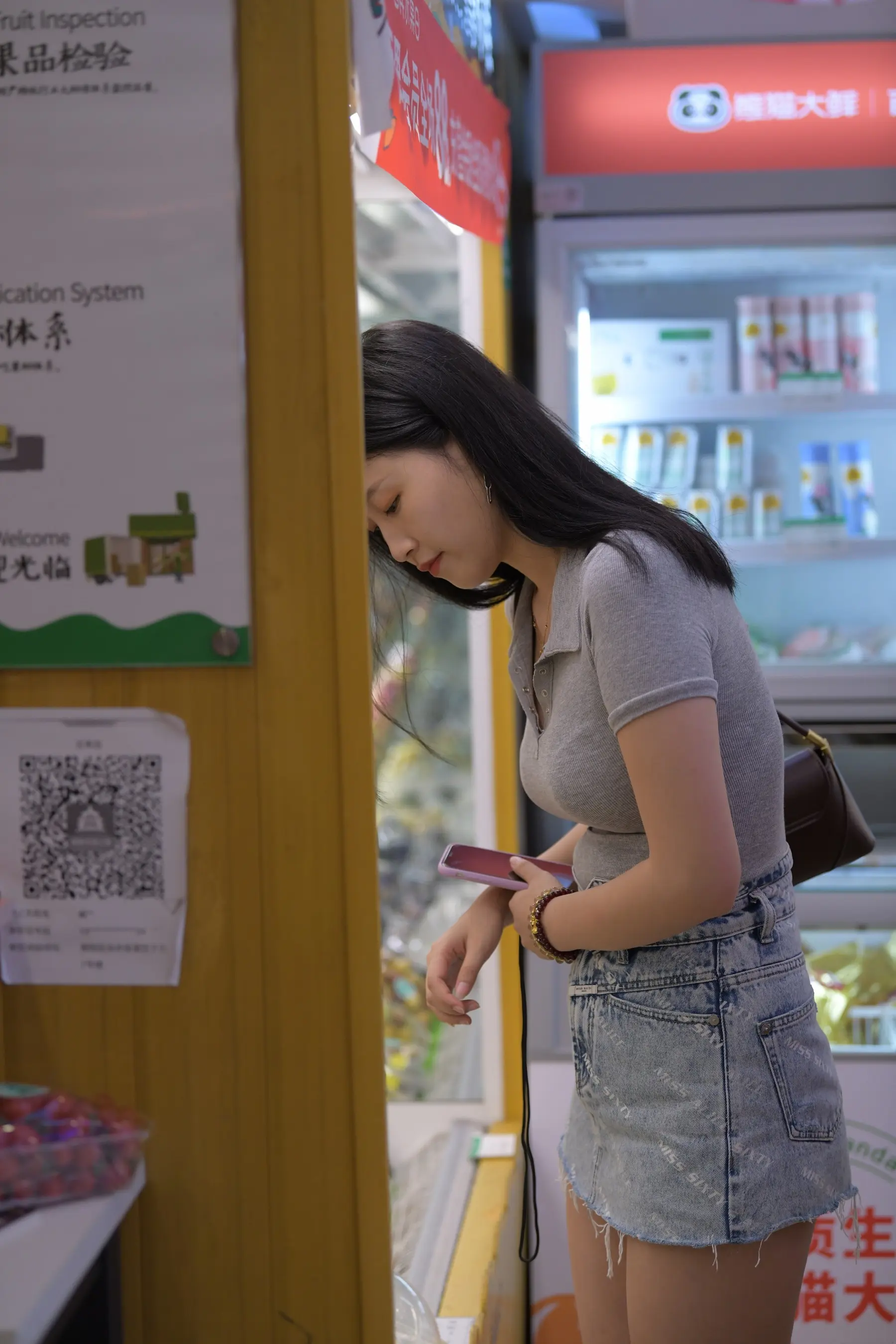 穿着灰色衬衫和牛仔裙的女人看着她的手机