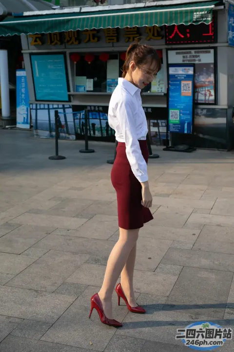 身穿红色裙子和白色衬衫的女子走在商店前的人行道上