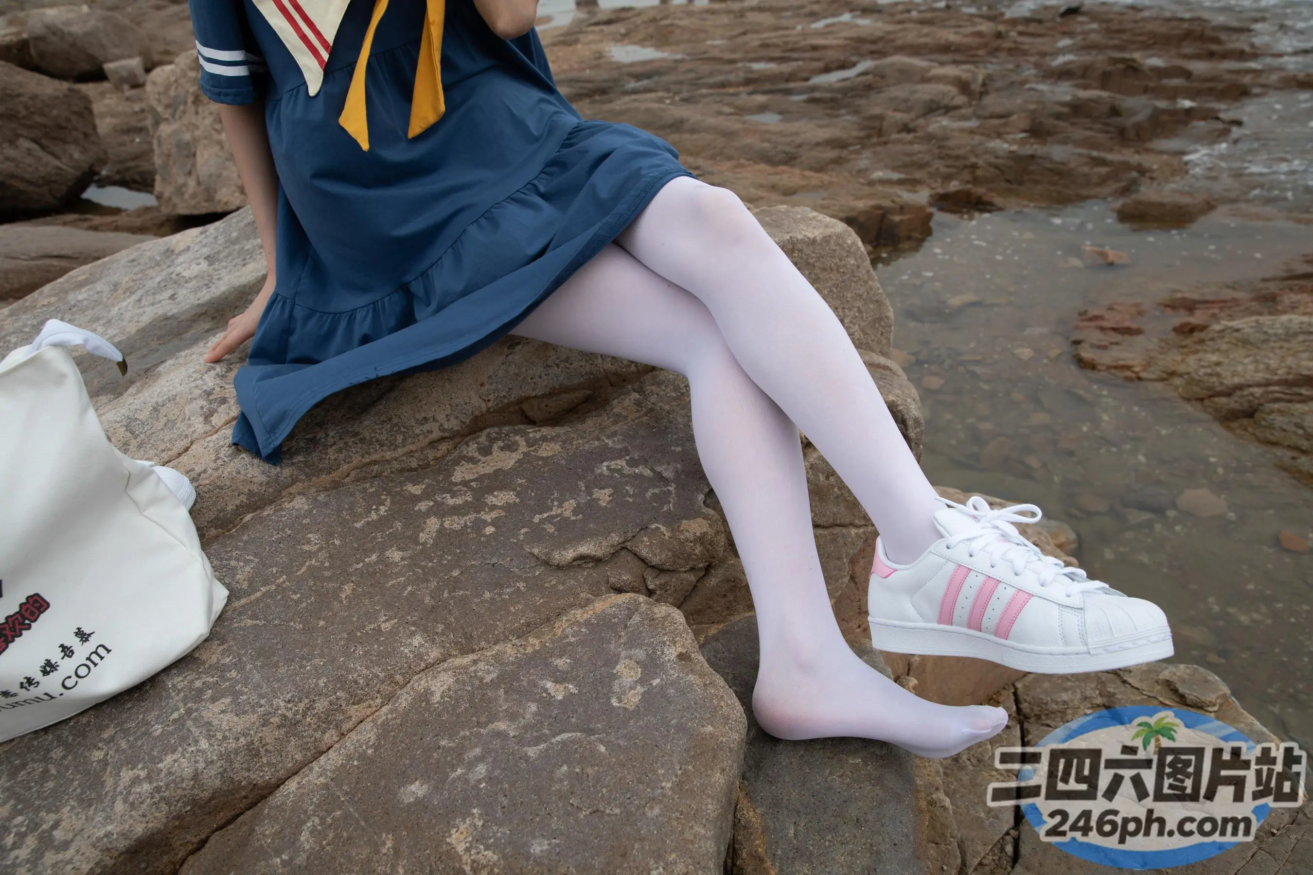 有一个女人坐在岩石上，戴着帽子，穿着一双白鞋