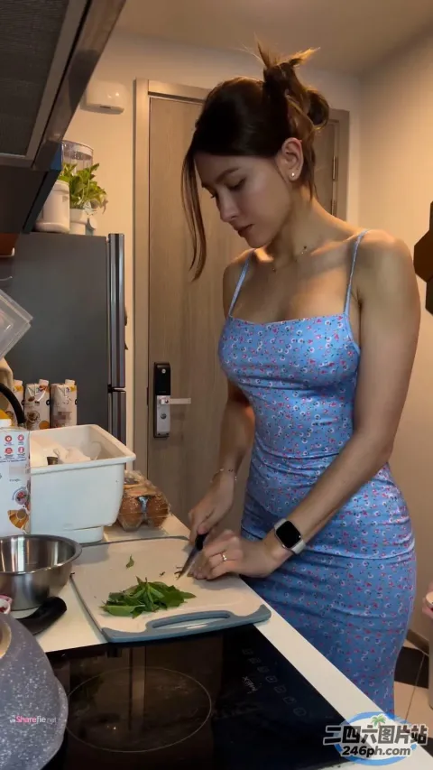 穿蓝色连衣裙的女人在厨房里切菜，厨房里有炉灶和冰箱