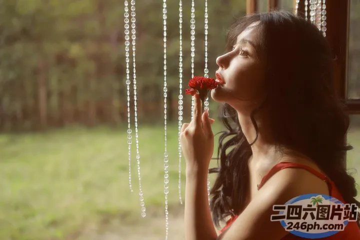 身穿红裙的 Araffe 女子在窗前闻花香